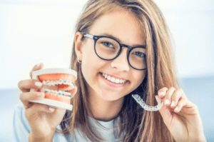 girl holding clear aligners and 3d model with braces invisalign cosmetic dentistry Virginia Beach Virginia